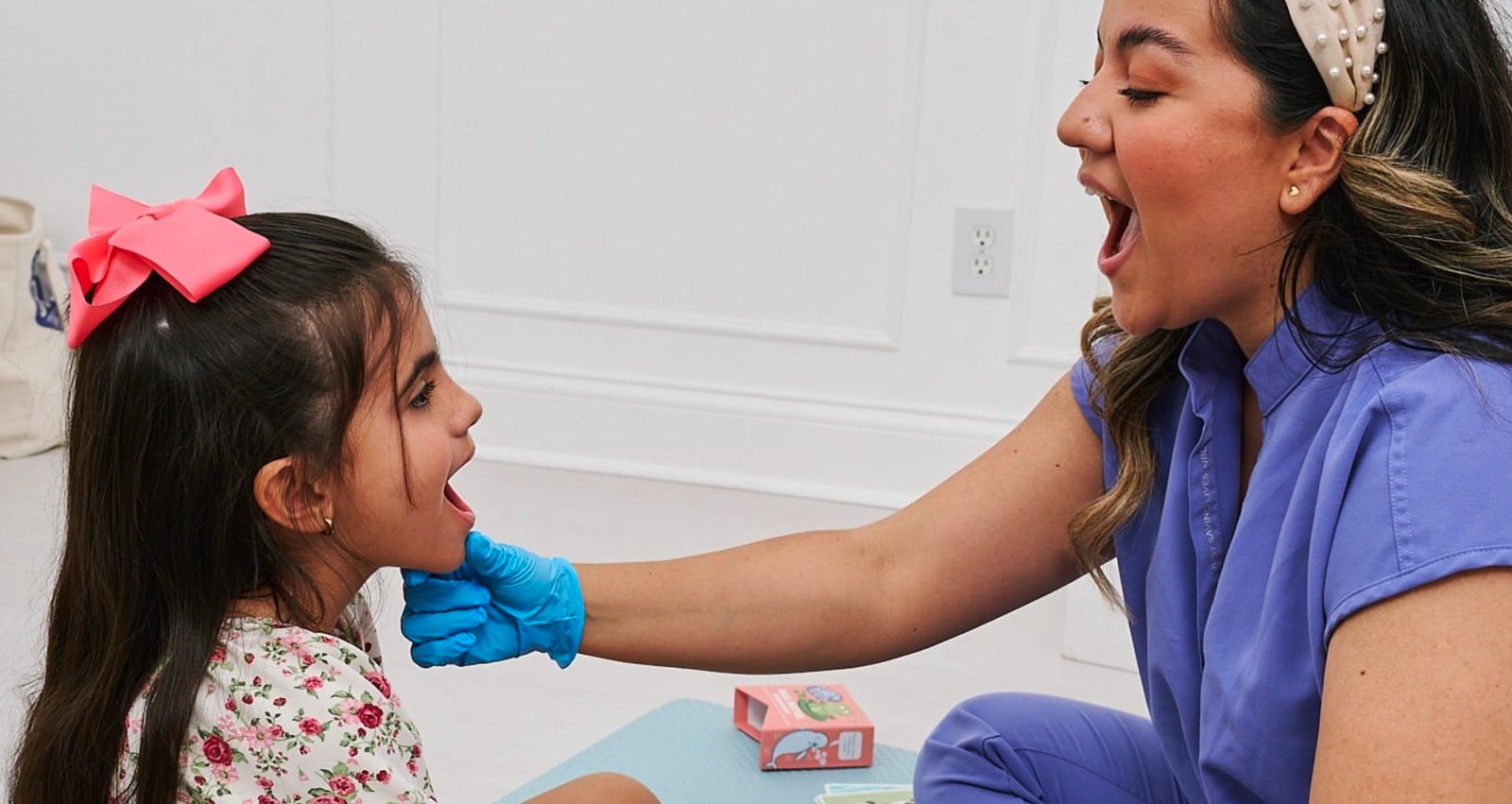 A speech therapist working with a young girl on the floor, in person
